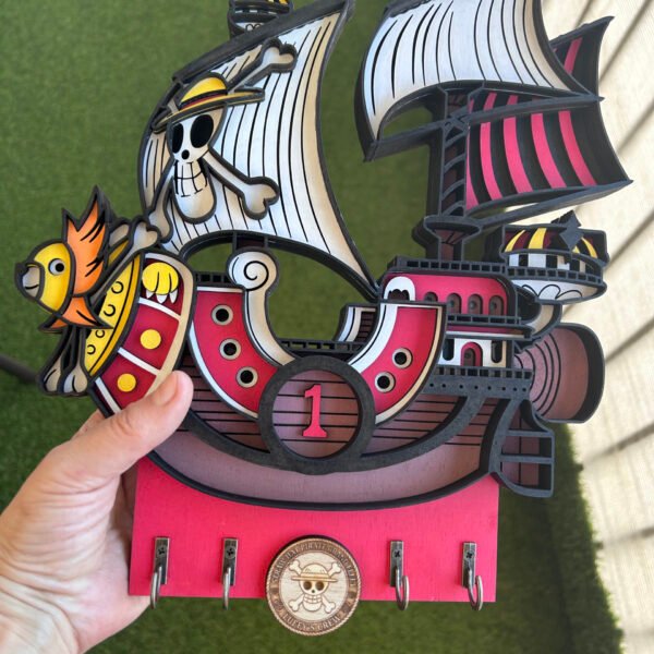 Colgador de llaves artesanal de madera 3D del barco One Piece Thousand Sunny, mostrando el modelo detallado en capas y los cuatro ganchos metálicos para llaves.